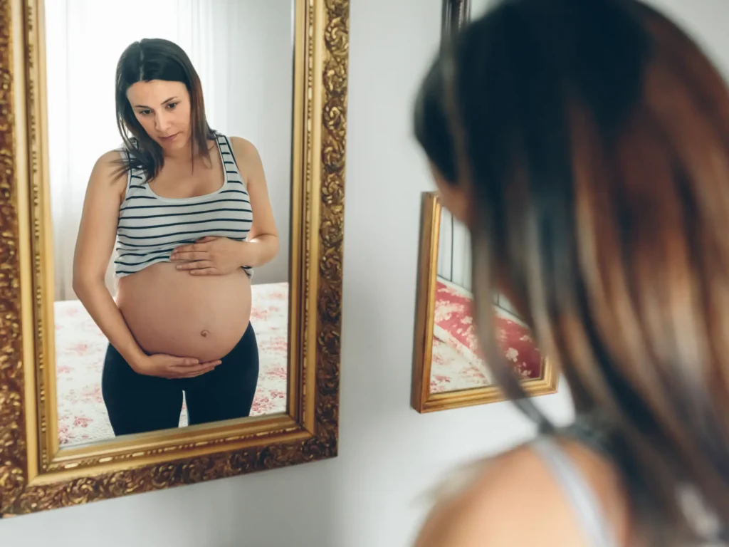 donna in gravidanza che si guarda allo specchio, è importante amarsi ed accettare il proprio corpo in gravidanza